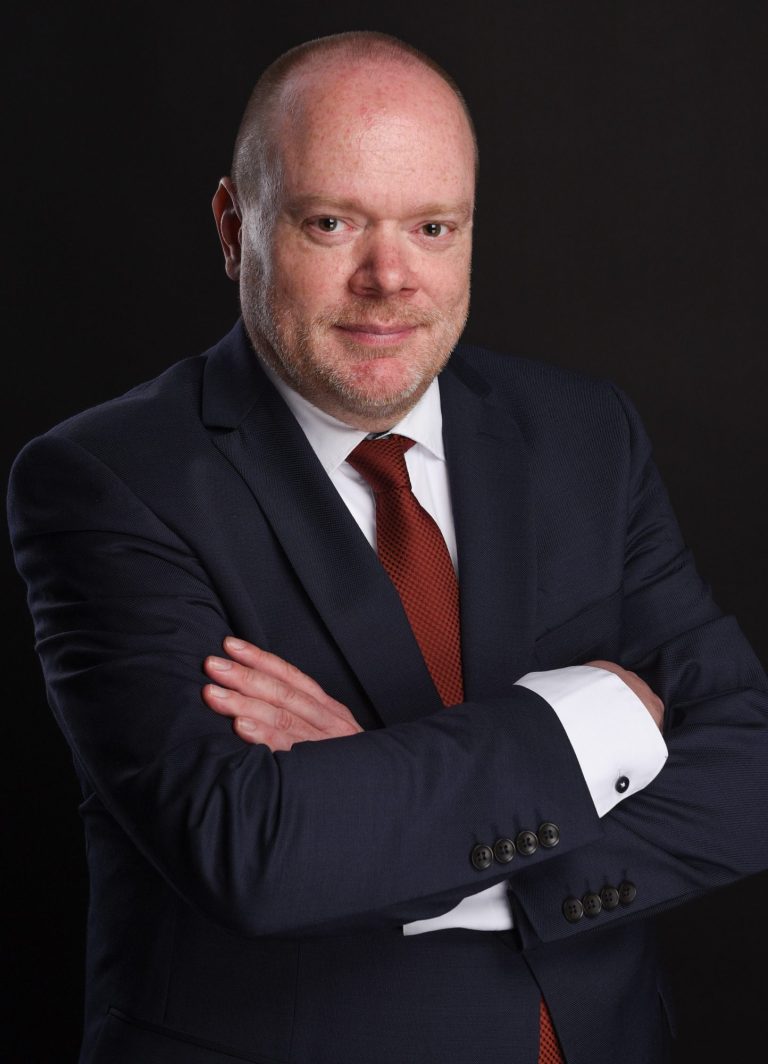 Bernd Fischer Ein Mann in einem Anzug mit verschränkten Armen, lächelnd vor einem hellen Hintergrund.